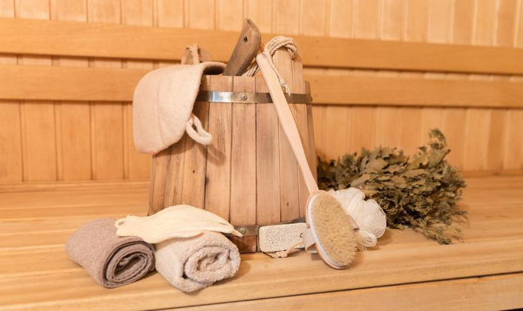 Body care items laid out on display: a long-handled wooden body brush, multiple wash cloths with different textures and weaves, and a steam room visual, illustrating various methods for body cleansing and wellness.